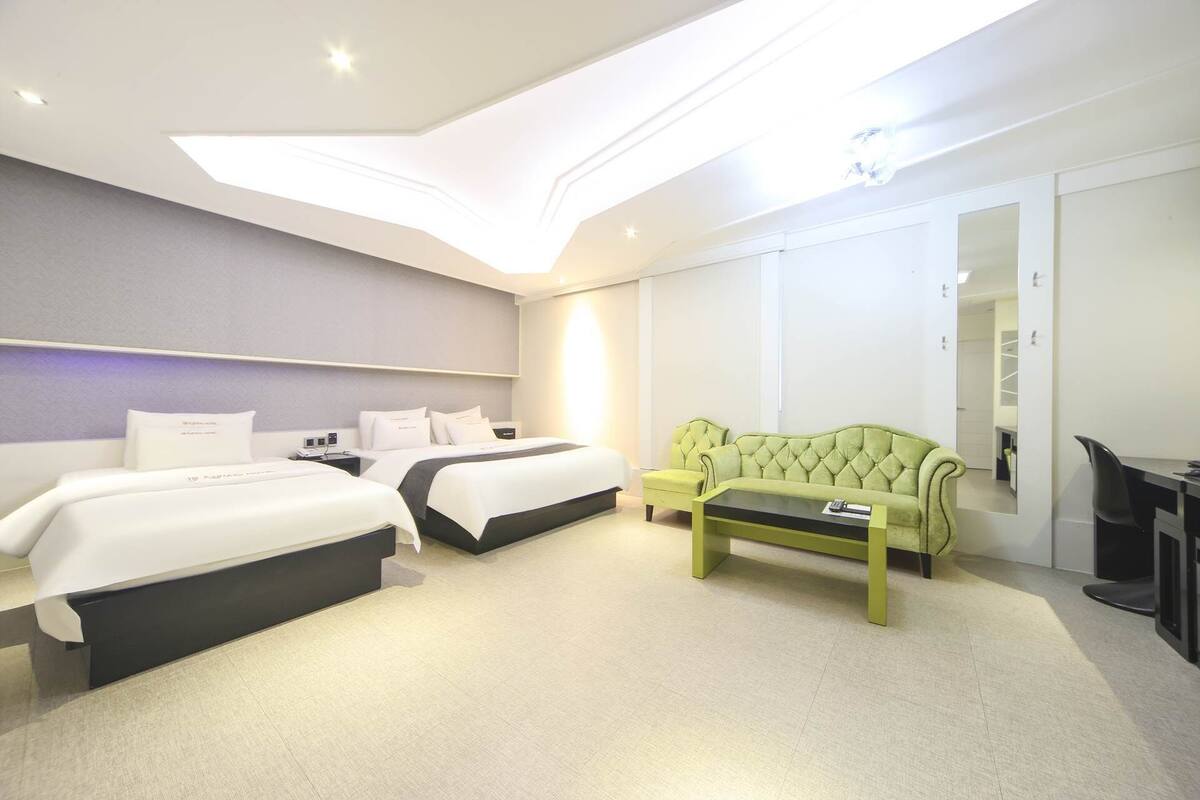 A hotel room with two beds, a green sofa, a desk, and a large mirror.