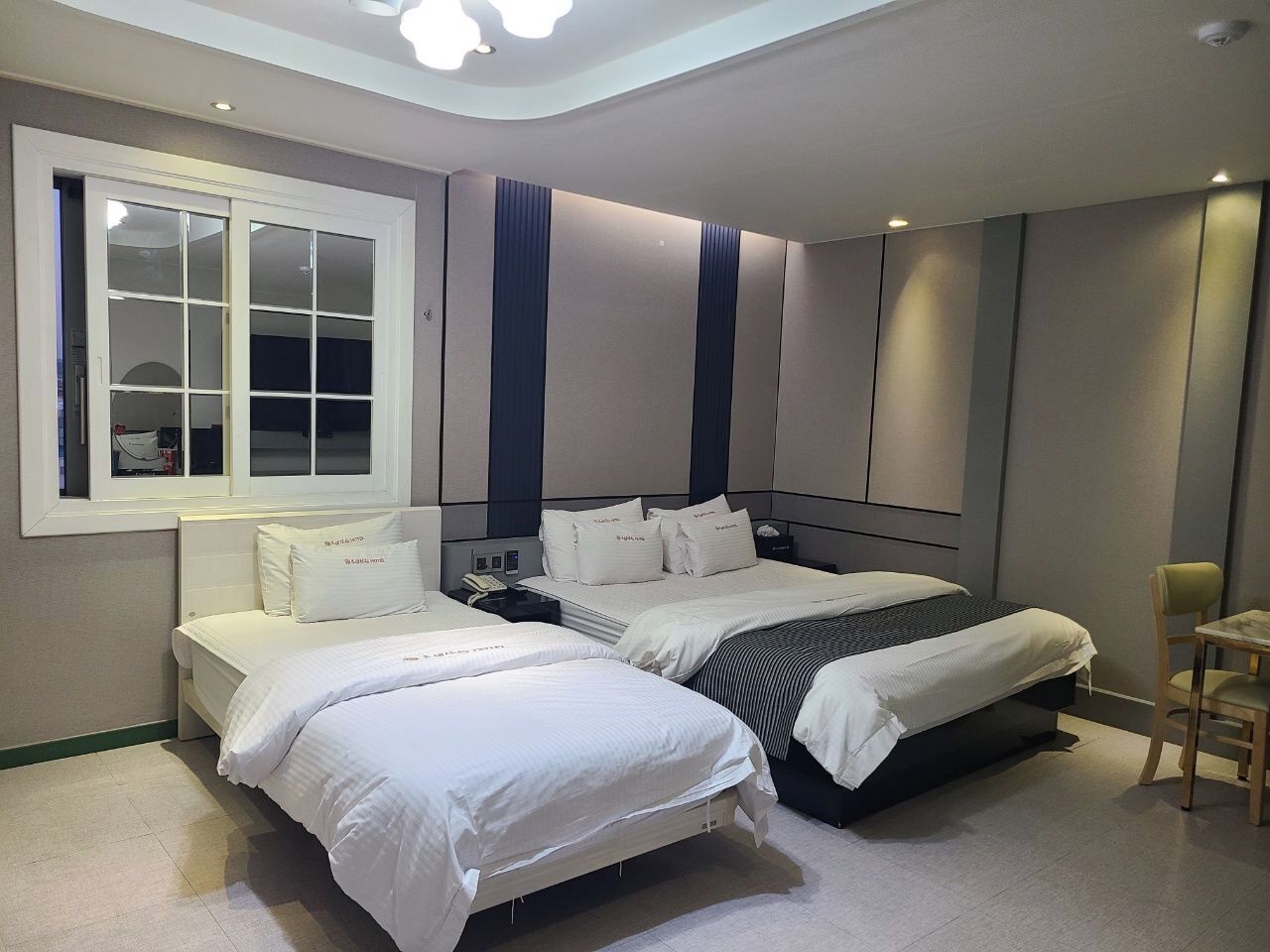 A modern bedroom with two beds, a window, and a desk.