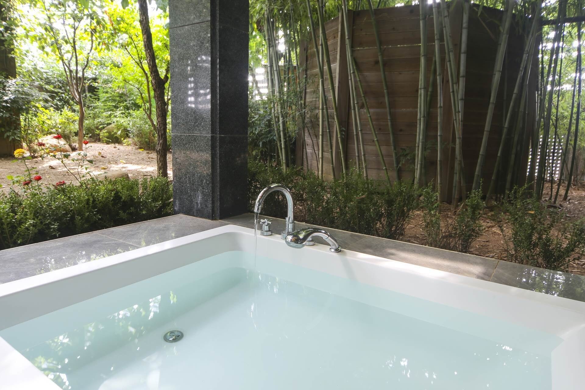 Een modern buitenbad met een achtergrond van een stenen muur, omringd door bamboe en groen.
