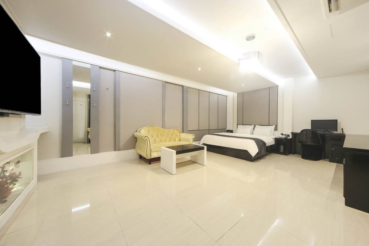 A modern hotel room with a large bed, a sofa, a desk, and a television.