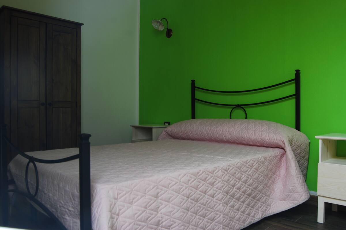 A bedroom with a bed, a nightstand, a wardrobe, and a green wall.
