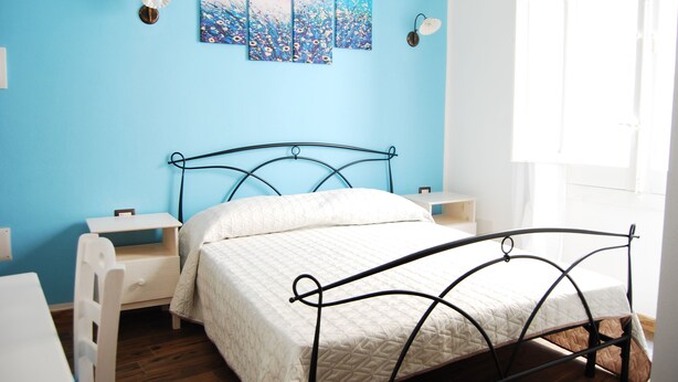 A bedroom with a bed, bedside tables, a nightstand, and a wall with three paintings. - Dani's House (Cagliari)