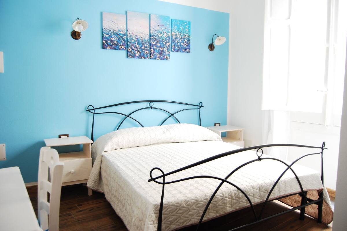 A bedroom with a bed, bedside tables, a nightstand, and a wall with three paintings.