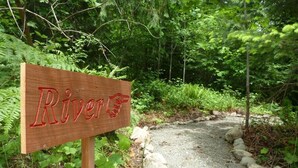 A wooden sign with the word "River" and a hand pointing towards it, surrounded by greenery and a gravel path.
