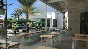 An outdoor cafe with tables and chairs, palm trees, and a building in the background. - 🦩Book Me Baby! Pool, Pet-Friendly Paradise Near Downtown Sarasota🦩 (Sarasota)
