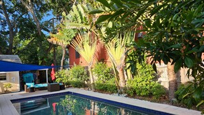 A swimming pool surrounded by lush greenery, a covered seating area, and a building with a red facade. - 🦩Book Me Baby! Pool, Pet-Friendly Paradise Near Downtown Sarasota🦩 (Sarasota)