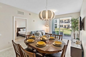 A dining area with a round table set for six, a ceiling light fixture, and a view of a balcony with a railing.