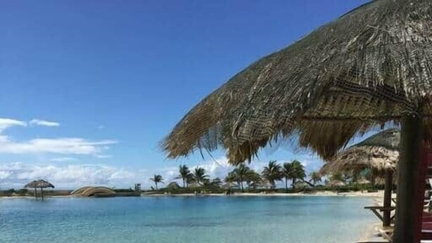 A beach with clear water, a thatched umbrella, and a wooden structure. - Añoranza 3 BDRM: 2 Bedroom Villa + Casita 2 (Punta Blanca)