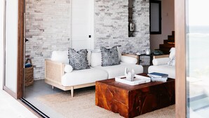 A modern living room with a white sofa, patterned cushions, a wooden coffee table, and a brick wall. - Añoranza 3 BDRM: 2 Bedroom Villa + Casita 2 (Punta Blanca)