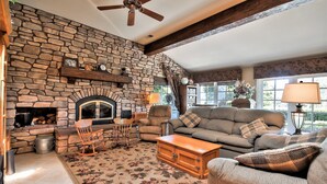 A cozy living room with a stone fireplace, wooden furniture, and a large window. - Fallbrook Tuscan villa oasis! (Fallbrook)