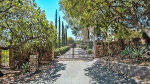 A paved pathway leading to a gated entrance with a stone wall and a metal gate. - Fallbrook Tuscan villa oasis! (Fallbrook)