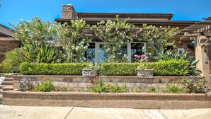 A building with a stone facade, a wooden pergola, and a landscaped garden with various plants and flowers. - Fallbrook Tuscan villa oasis! (Fallbrook)