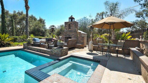A swimming pool with a stone structure, outdoor seating, and surrounding greenery. - Fallbrook Tuscan villa oasis! (Fallbrook)