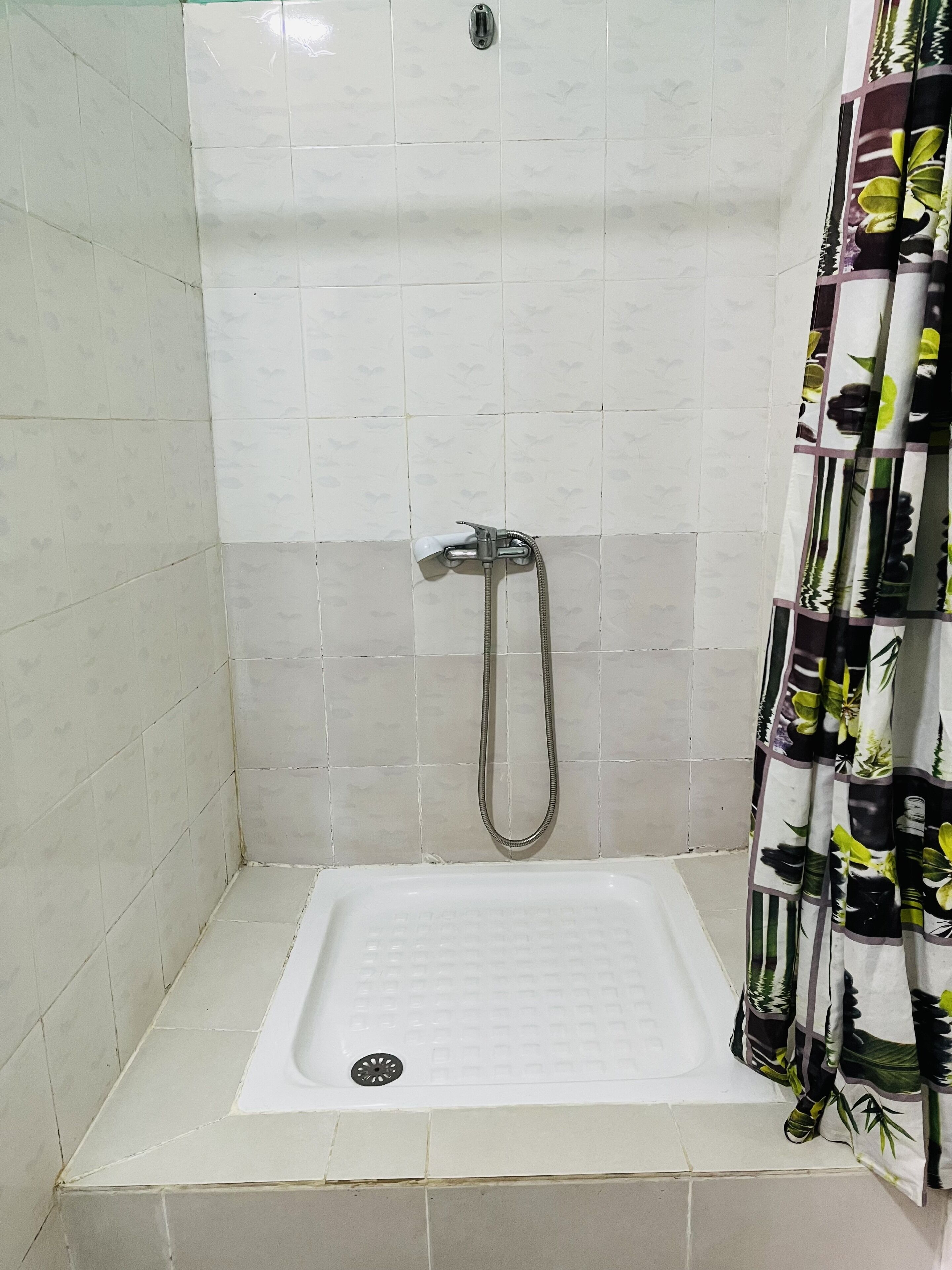 A small, white-tiled shower stall with a showerhead and a drain.