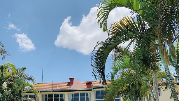 A pool area with lounge chairs, a building with large windows, and palm trees. - Hotel Appartement meublé Les Flots Bleu (Antananarivo)