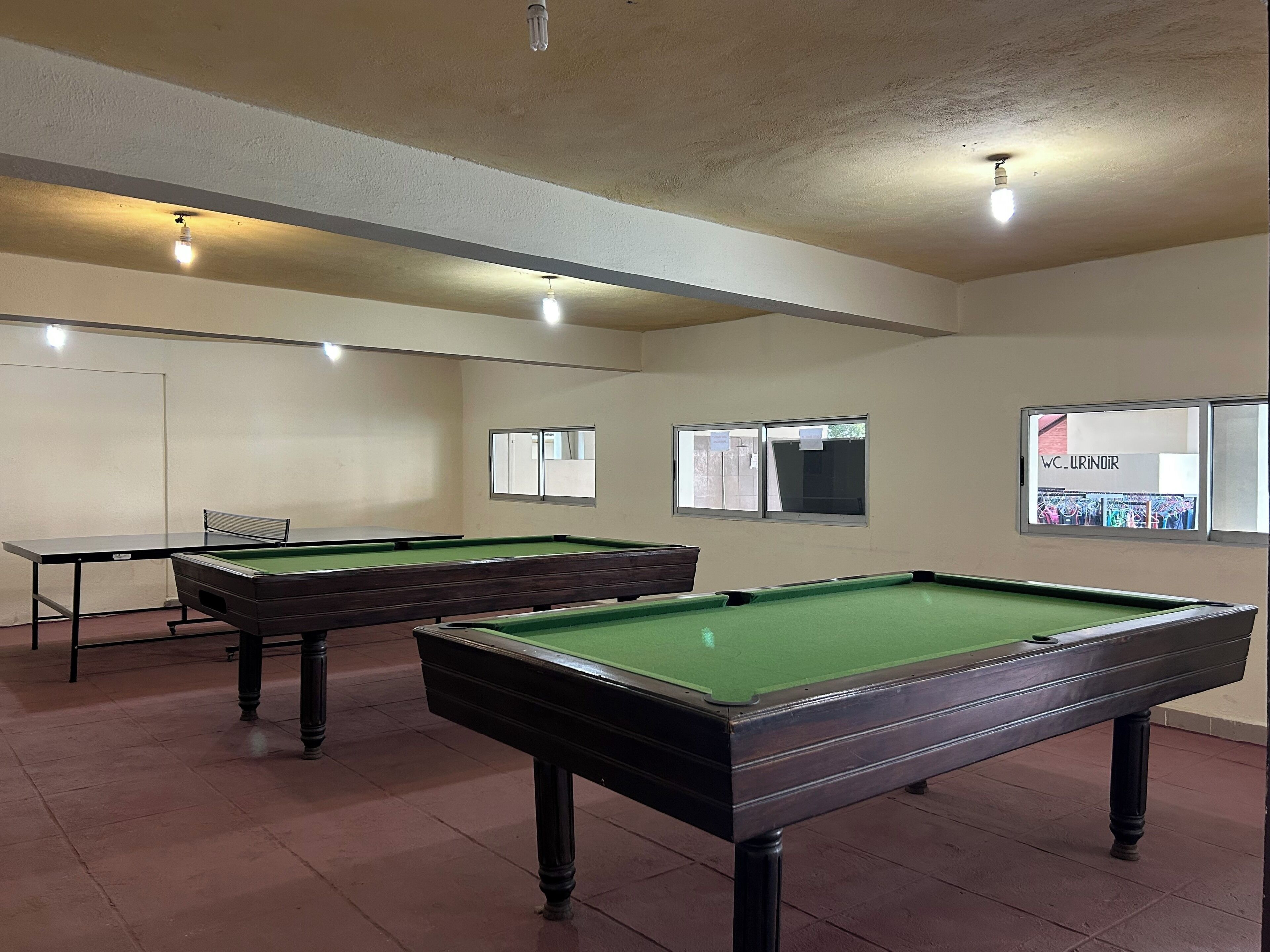 A pool hall with two pool tables, a billiard table, and a window with a poster.
