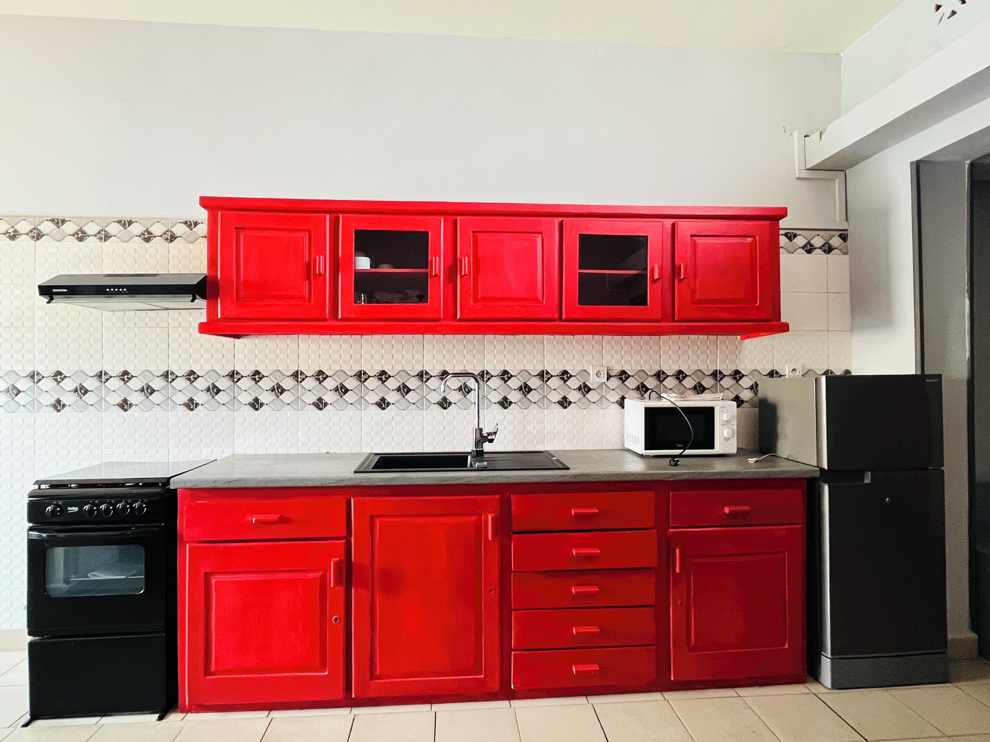 Una cocina con gabinetes rojos, un microondas, una estufa y un refrigerador.