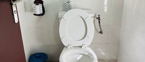 Un baño con un inodoro blanco, un bote de basura azul y un dispensador de papel higiénico en la pared.