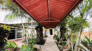 A covered pathway leading to a building with a glass entrance, surrounded by various potted plants and greenery. - Hotel Appartement meublé Les Flots Bleu (Antananarivo)