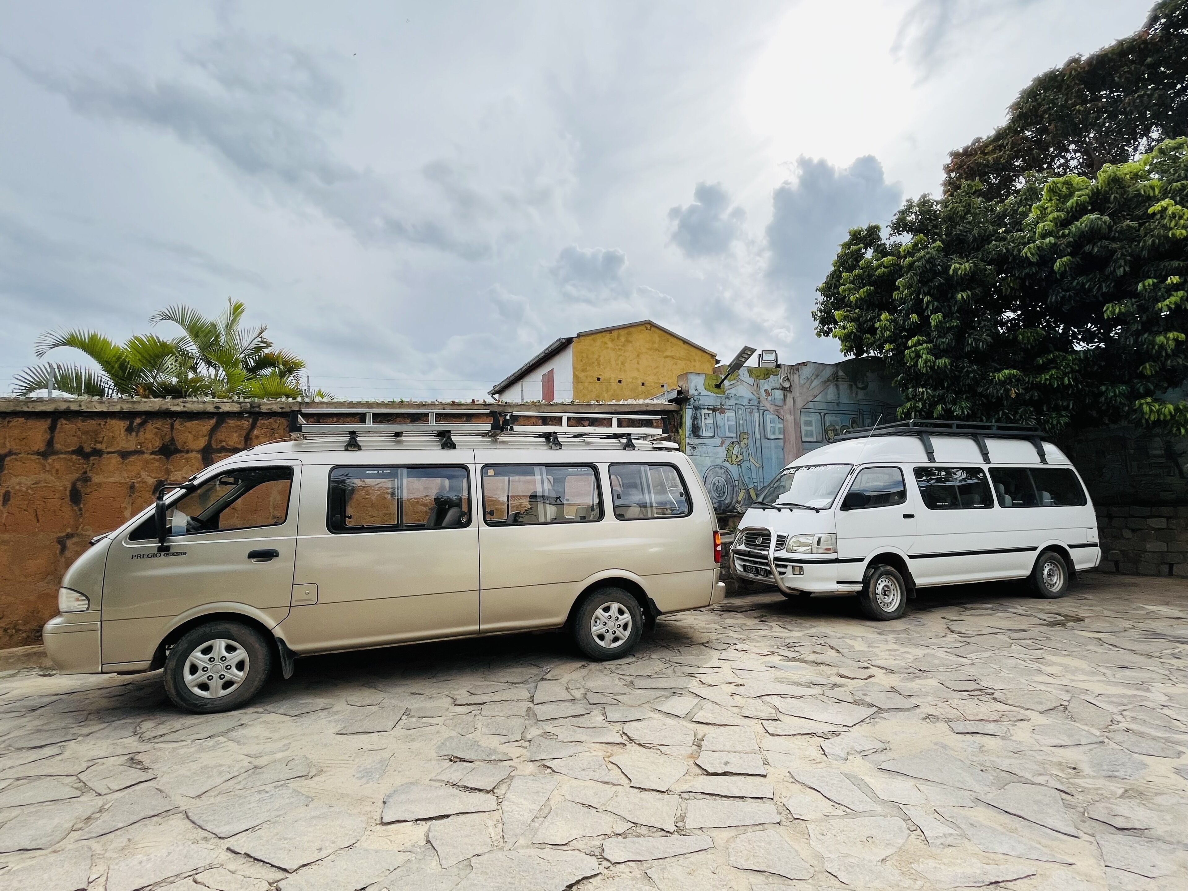 Two vans parked on a stone-paved area with a mural and a building in the background.