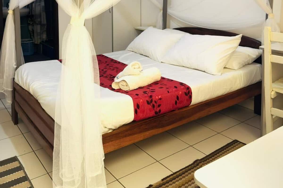 Una cama con dosel y cuatro columnas, con ropa de cama blanca y una manta roja.