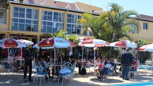 A poolside area with outdoor seating and umbrellas, surrounded by palm trees and a building with large windows. - Hotel Appartement meublé Les Flots Bleu (Antananarivo)