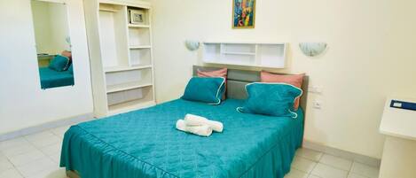 Un dormitorio con cama, almohadas, una mesita de noche, un espejo y una estantería.