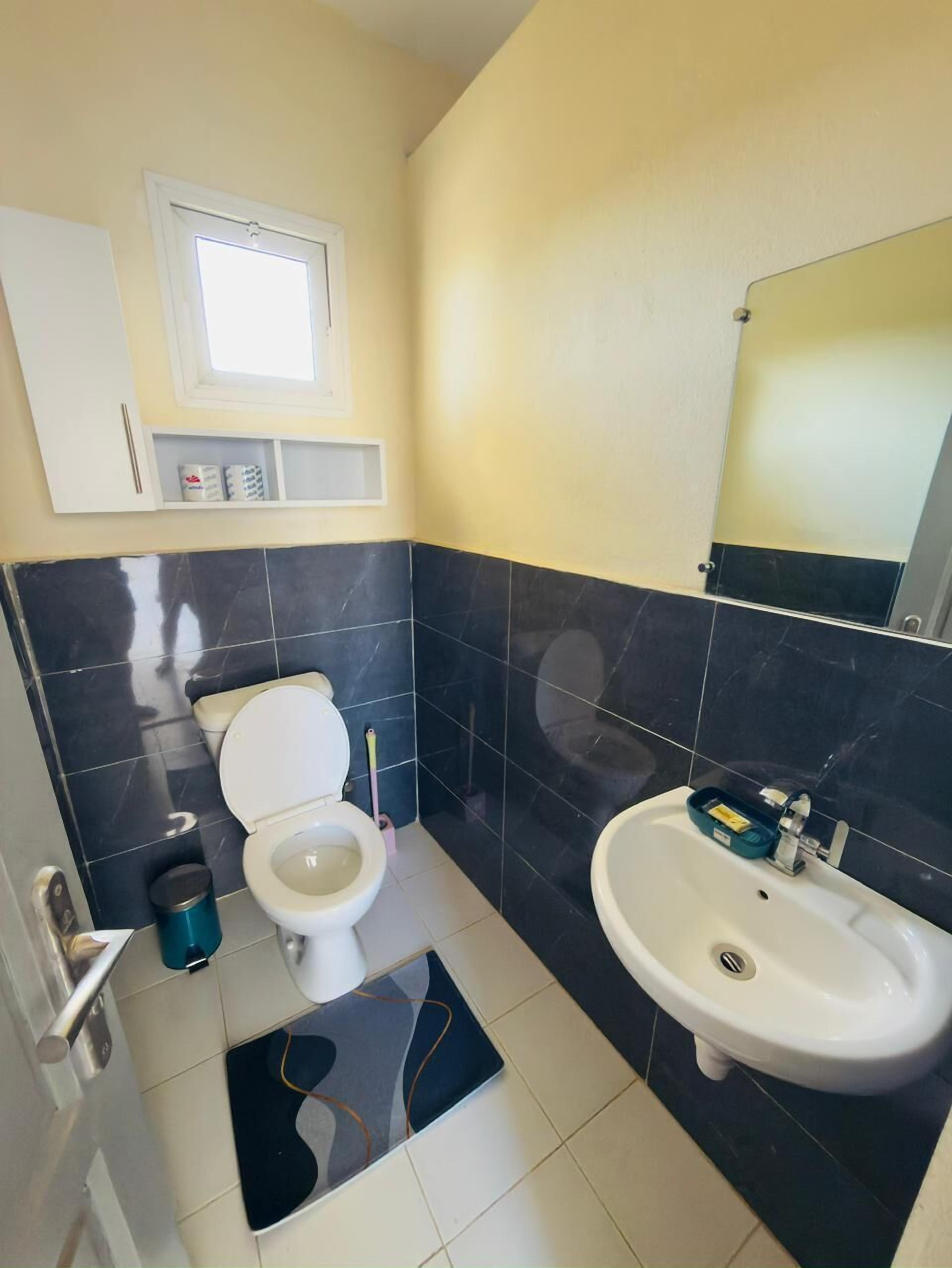 Une salle de bain avec des toilettes, un lavabo et une fenêtre située au-dessus des toilettes.