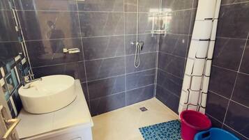 Et badeværelse med vask, toilet og brusebad samt et lille vindue.