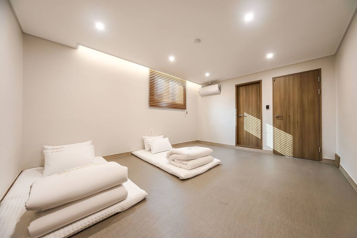 A modern, well-lit room with a large bed, a small seating area, and a wooden door.
