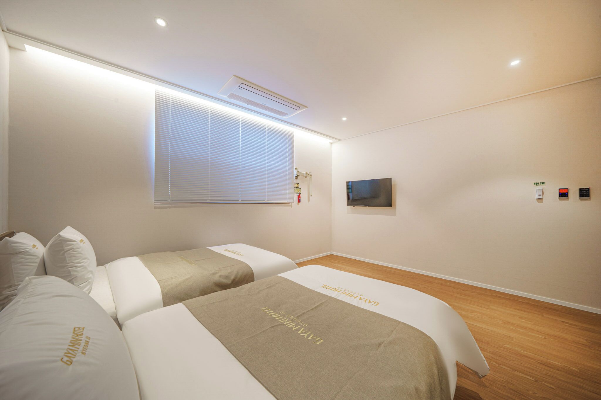 Habitación de hotel con dos camas, un televisor montado en la pared y una ventana con persianas.