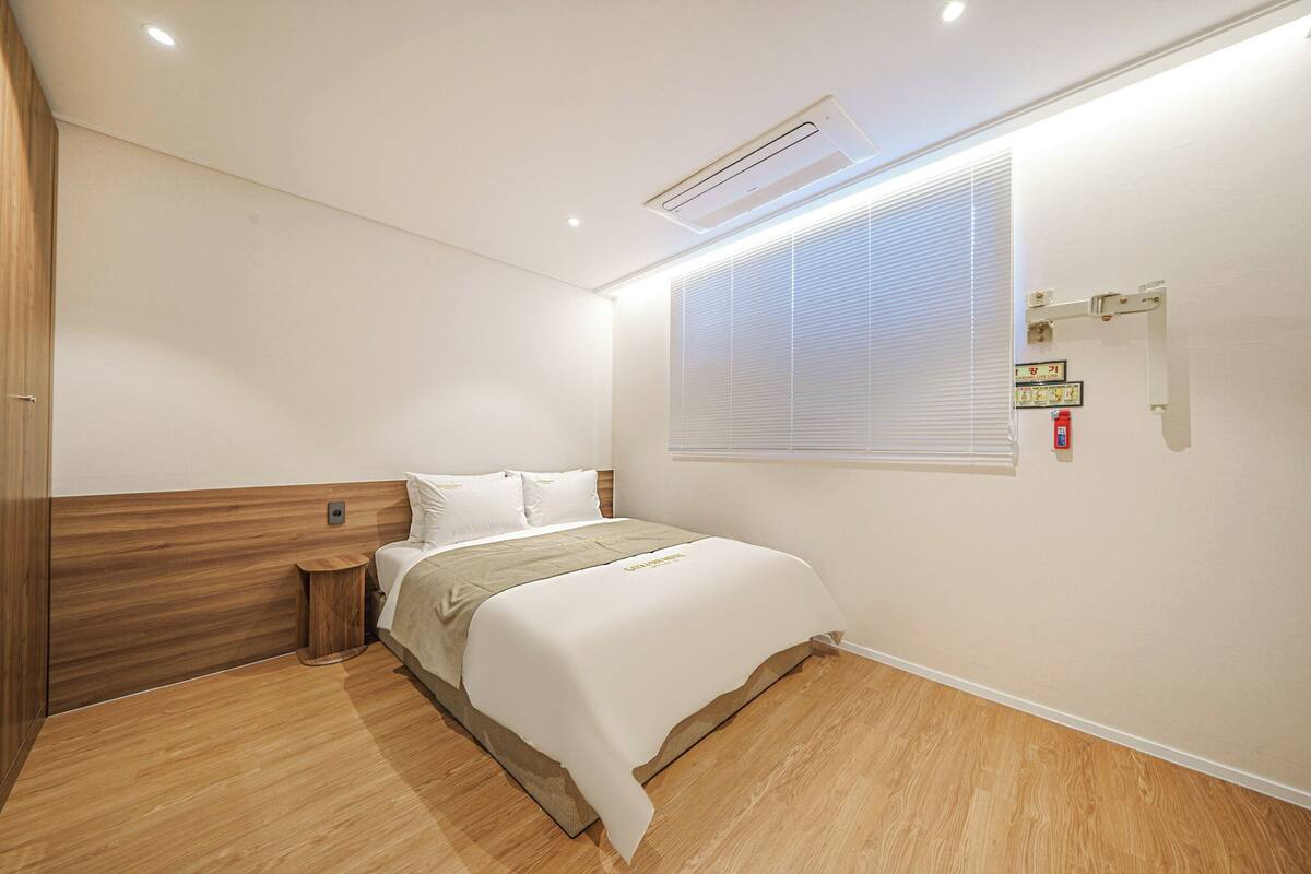 A modern bedroom with a wooden headboard, a single bed, a bedside table, and a window with blinds.