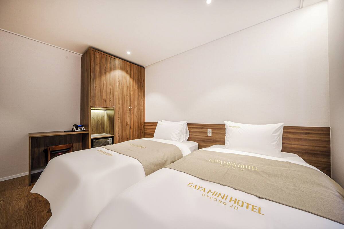 A hotel room with two beds, a wooden wardrobe, a desk, and a chair.