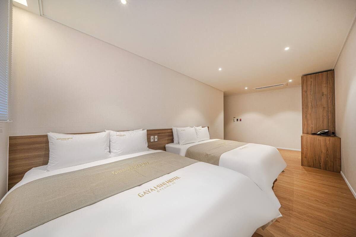 A hotel room with two beds, a wooden headboard, and a small wooden cabinet with a phone.