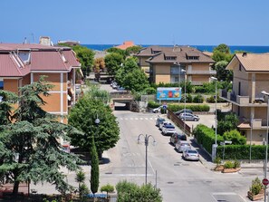 A residential street with houses, parked cars, and a clear view of the sea.