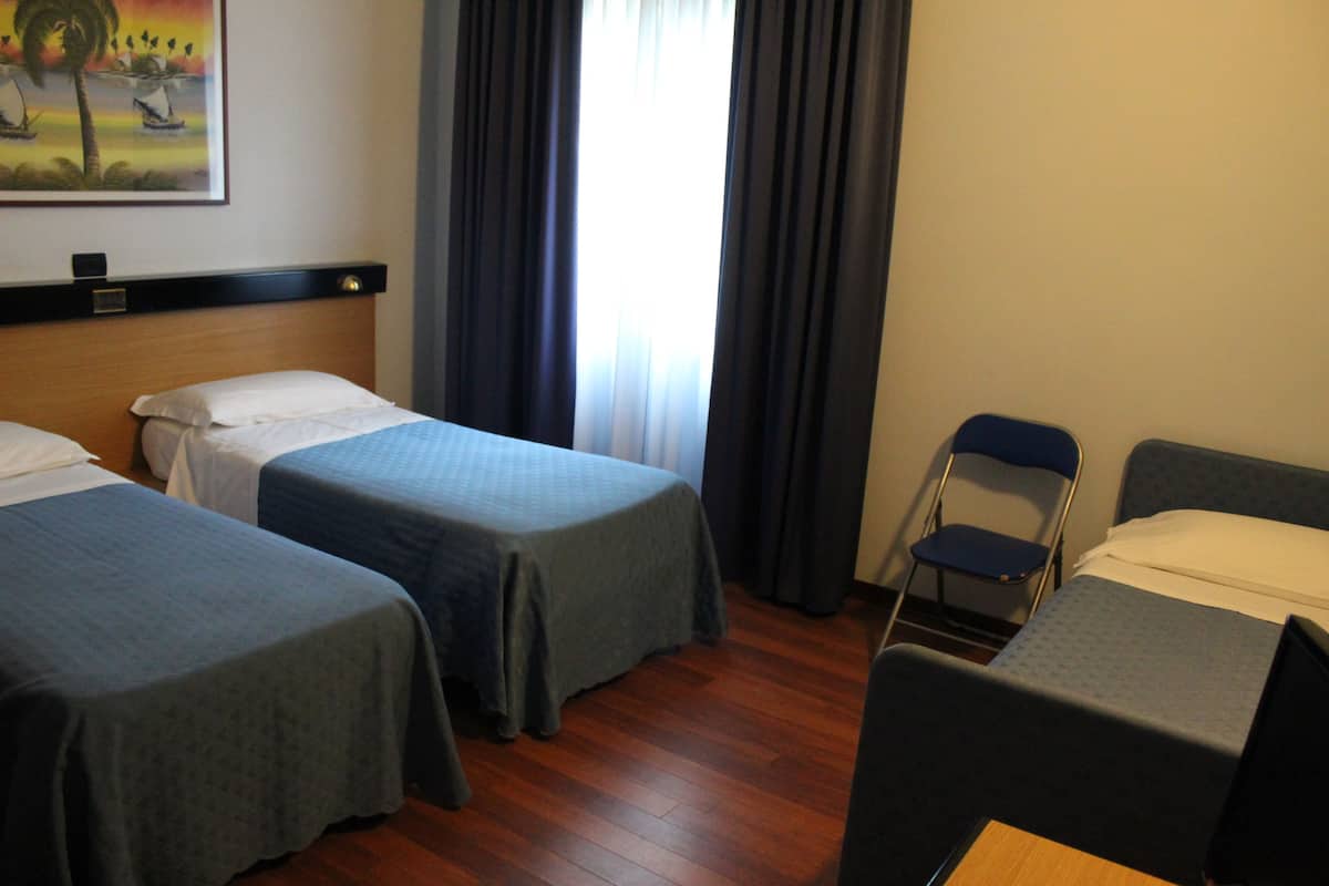 A hotel room with two single beds, a wooden floor, a chair, and a painting on the wall.