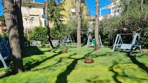 Uma área gramada bem cuidada com balanços e um pequeno jardim.