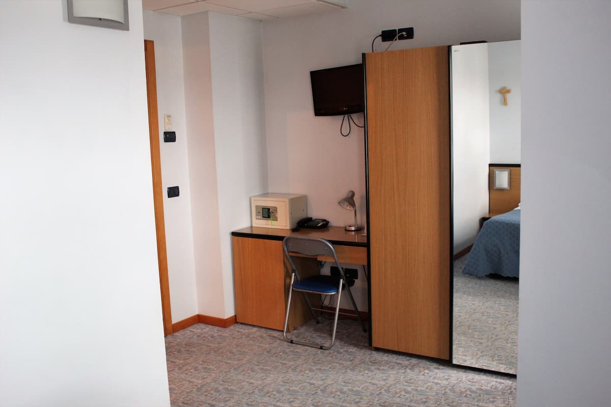 A small room with a desk, chair, bed, and a television mounted on the wall.