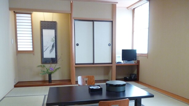 A traditional Japanese room with tatami flooring, a low table, a chair, a television on a shelf, and a framed artwork on the wall. - Hotel Hashimotorou (Ishioka)