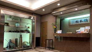 A reception area with a glass display case containing decorative items, a reception desk with a sign, and a tiled floor. - Hotel Hashimotorou (Ishioka)