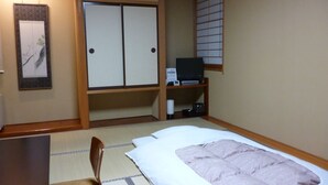 A traditional Japanese-style room with tatami flooring, a bed with a pink blanket, a desk with a chair, a television, and a cabinet with a small shelf. - Hotel Hashimotorou (Ishioka)
