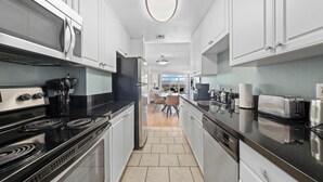 Een moderne keuken met witte kasten, een zwart aanrecht, roestvrijstalen apparatuur en uitzicht op de eethoek.