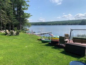 A lakeside deck with outdoor seating, a dock, and a grassy area.