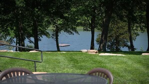 A lakeside patio with a table and chairs, surrounded by trees and a dock. - Great Views | Lakeside | Family-Friendly Barn | Reunions, Events, Retreats (Rolla)