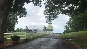 A rural road leading to a white farmhouse with a large barn, surrounded by trees and a white fence. - Great Views | Lakeside | Family-Friendly Barn | Reunions, Events, Retreats (Rolla)