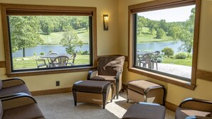 A room with large windows overlooking a lake, furnished with wicker chairs and ottomans. - Great Views | Lakeside | Family-Friendly Barn | Reunions, Events, Retreats (Rolla)