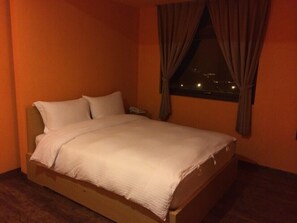 Un letto singolo in una stanza con pareti arancioni, una finestra con tende e vista notturna.