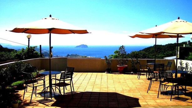 An outdoor patio with tiled flooring, round tables, chairs, and large umbrellas providing shade. - J.F Sleepless Ones Garden Hotel (New Taipei City)