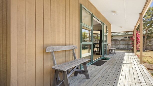 Una terraza de madera con un banco, un ventanal de vidrio y un espacio cubierto con una mesa y sillas.