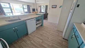 Una cocina compacta con armarios azul verdoso, lavavajillas y refrigerador.